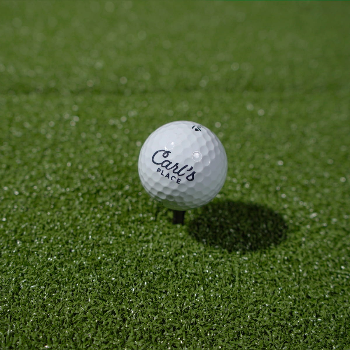 Carl's Place HotShot™ Hitting Mat - close-up of a branded golf ball teed up on the green turf hitting surface