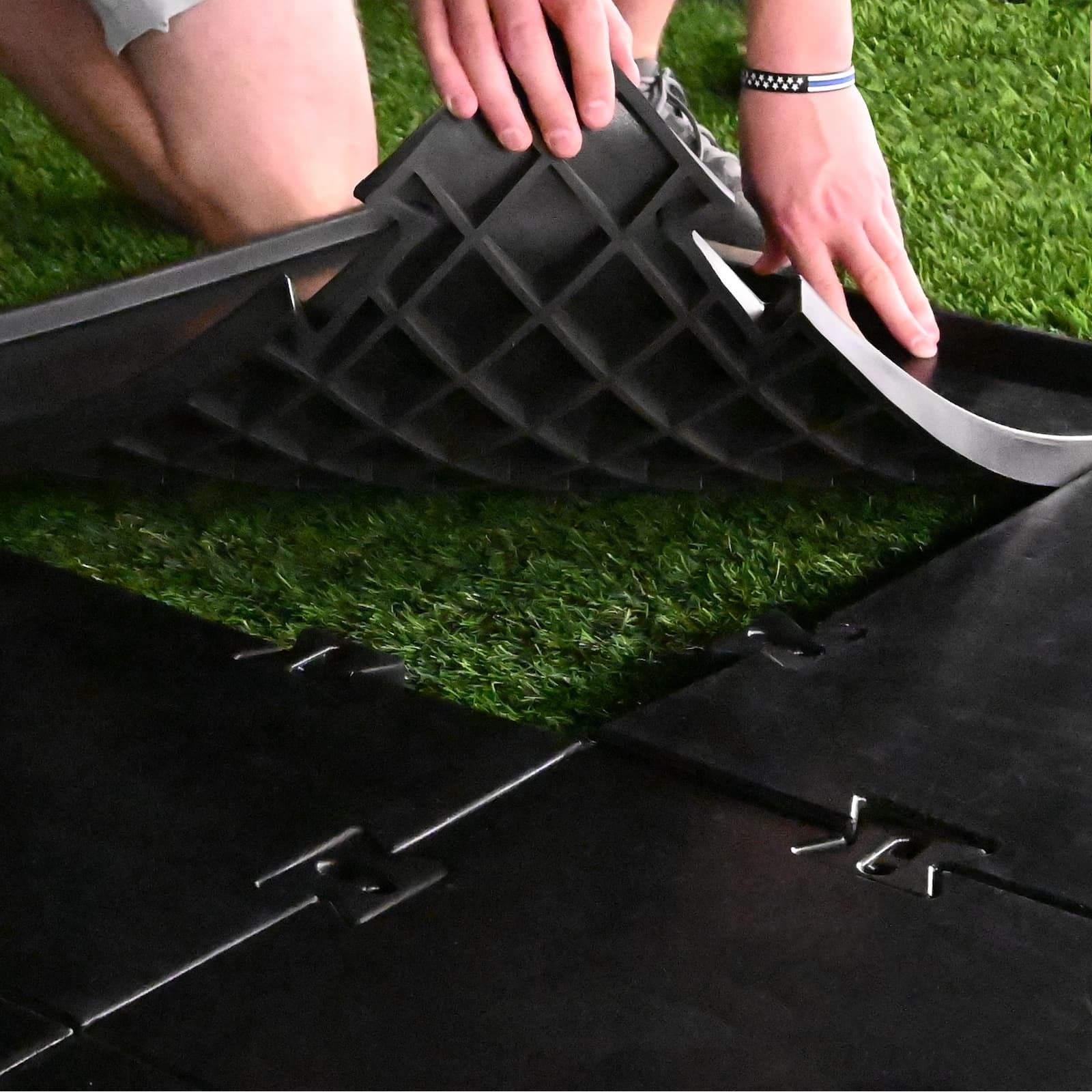 Carl's Place HotShot™ Golf Mat Base - hands lifting a panel to reveal its ribbed underside over green turf