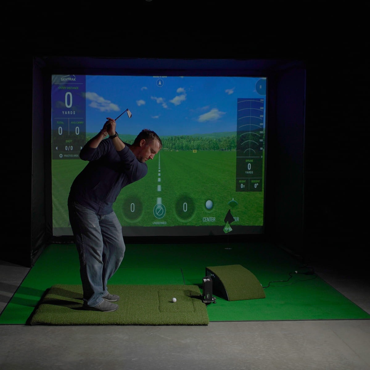 Carl's Place HotShot™ Hitting Mat - golfer at the top of a backswing on the mat facing a lit simulator screen